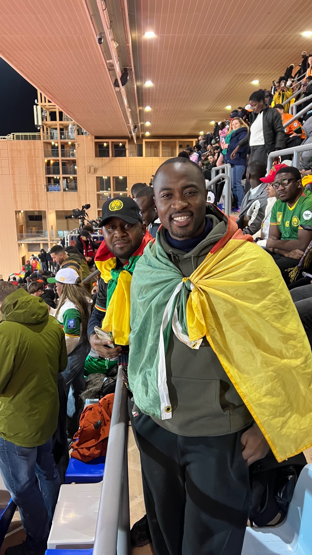 Two supporters in Cameroon colors smiling in the stadium