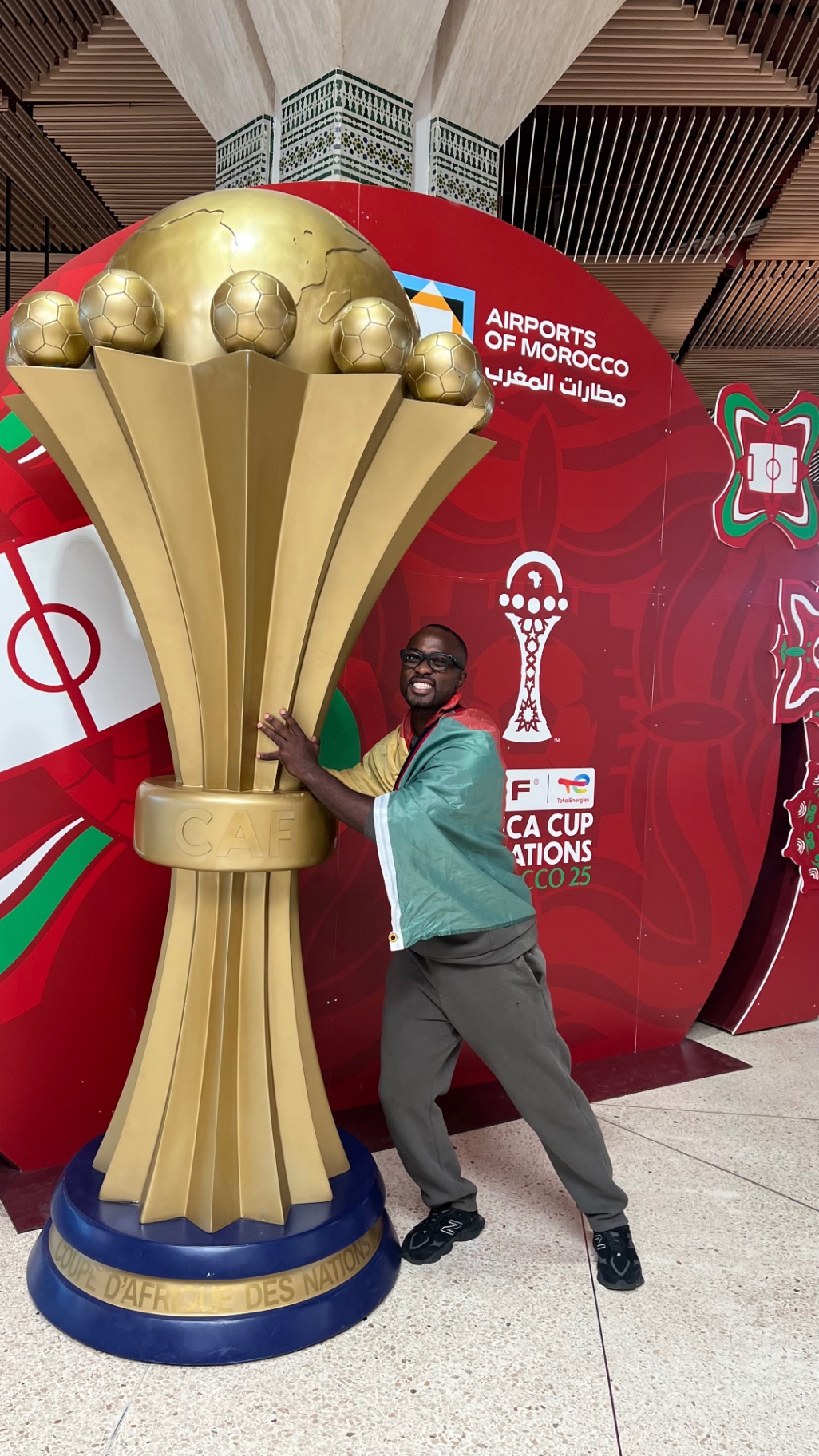 Traveler posing beside the Africa Cup of Nations trophy display at the airport in Morocco