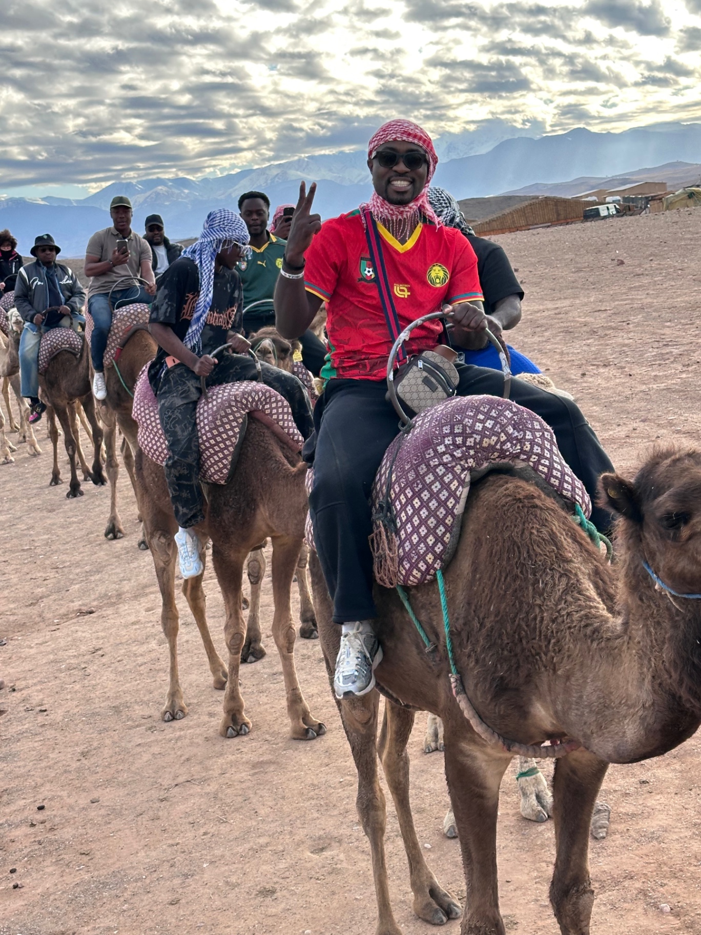 Traveler wearing a Cameroon jersey riding a camel with friends in Morocco